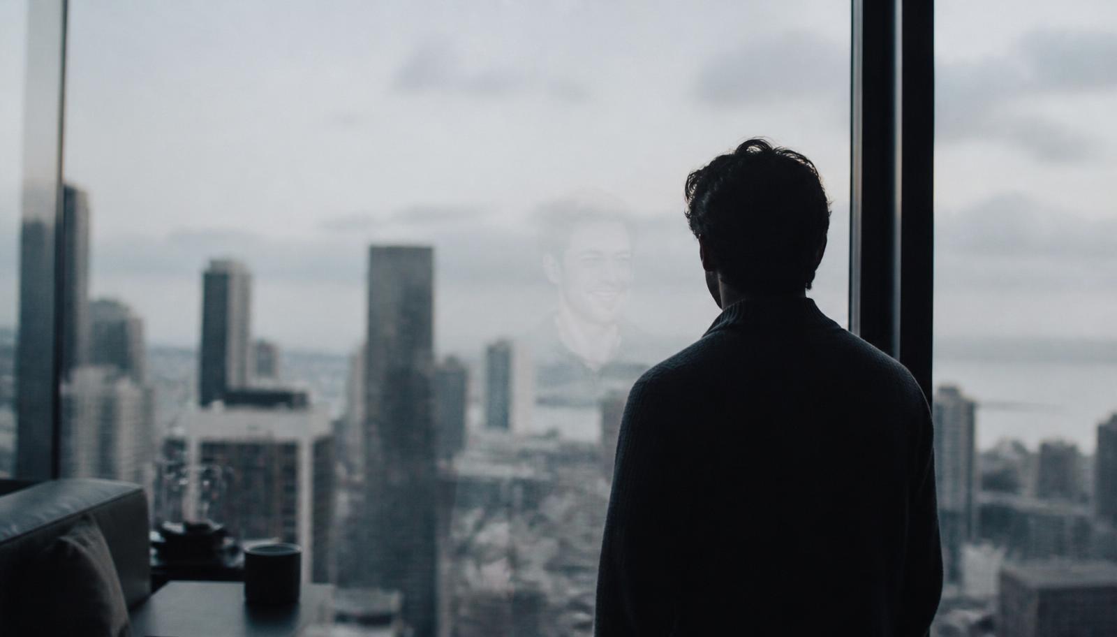 Silueta de una persona mirando por un gran ventanal con luz gris